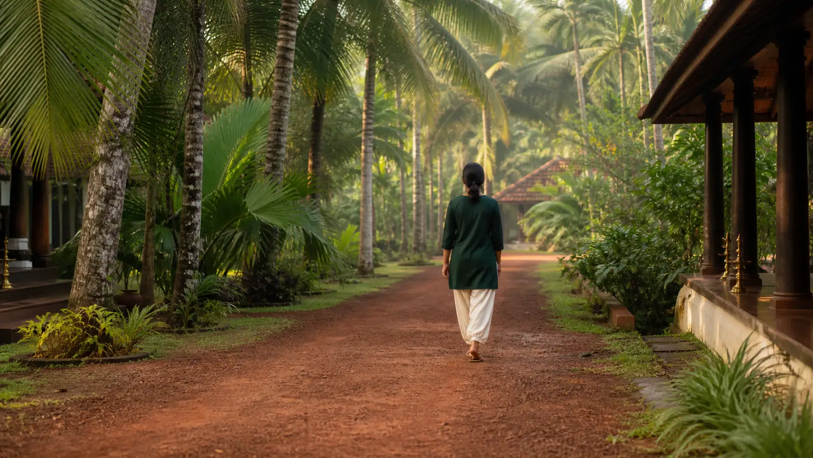A woman on an unhurried morning walk along a palm-lined path at a Kerala Ayurveda resort